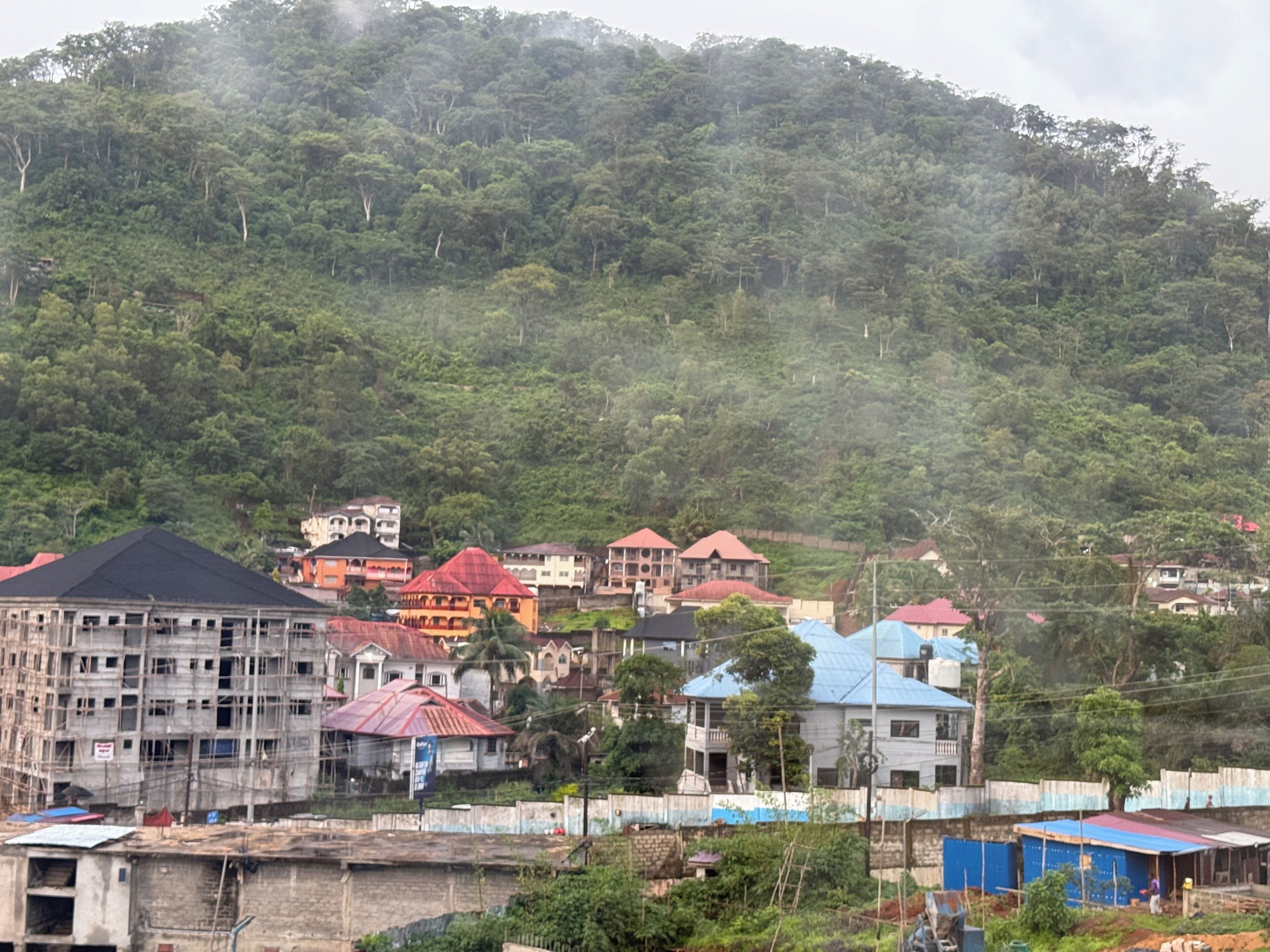 A residential area with houses on a hillside, some under construction, and a mix of building styles.