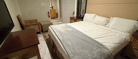 Habitación de hotel con cama, escritorio, silla, espejo y puerta que da a otra habitación.