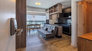 Una cocina moderna con electrodomésticos integrados, un comedor con mesa y sillas de madera, y un sofá gris en un amplio salón.
