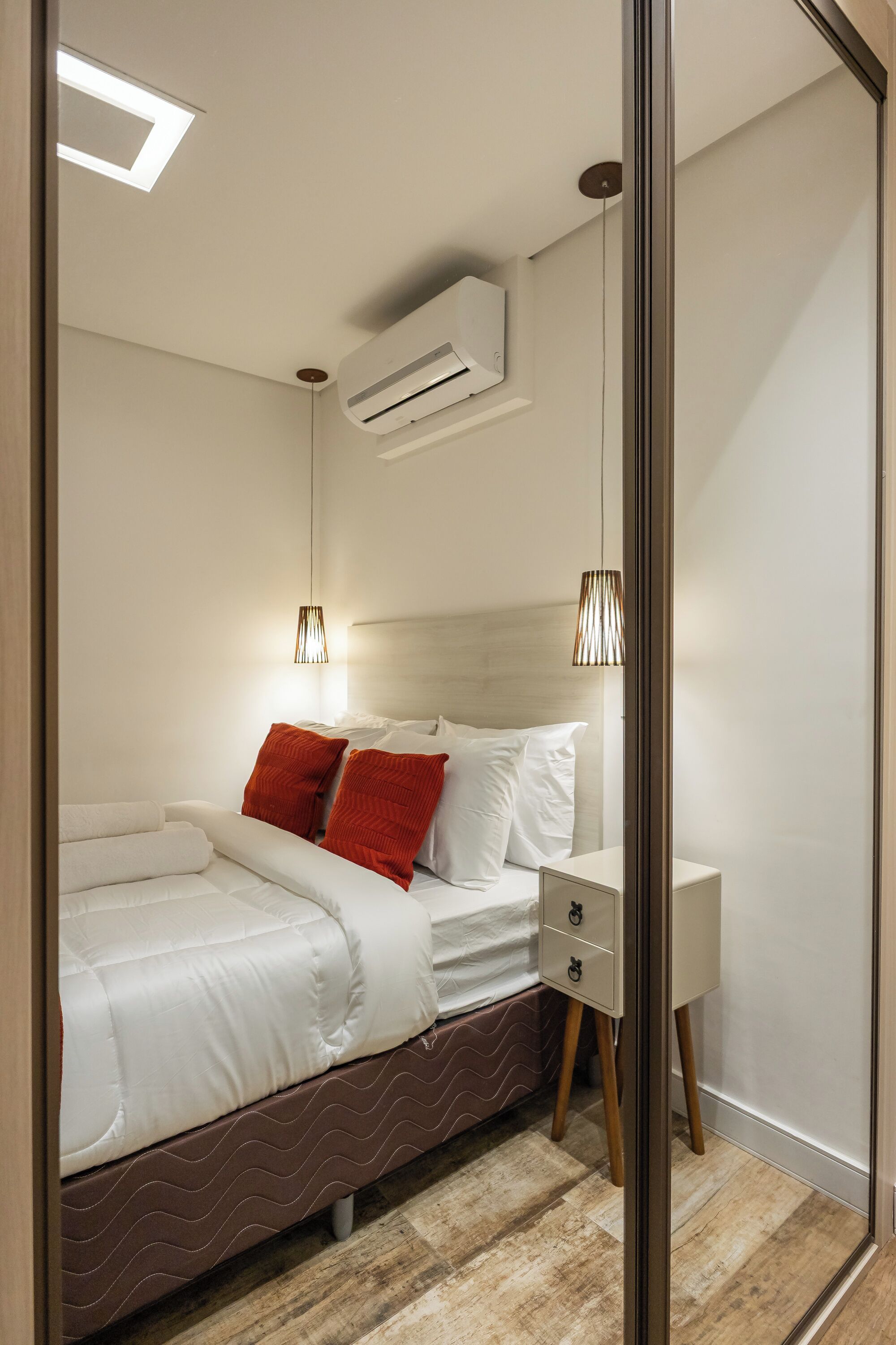 A modern bedroom with a bed, nightstand, and an air conditioning unit.