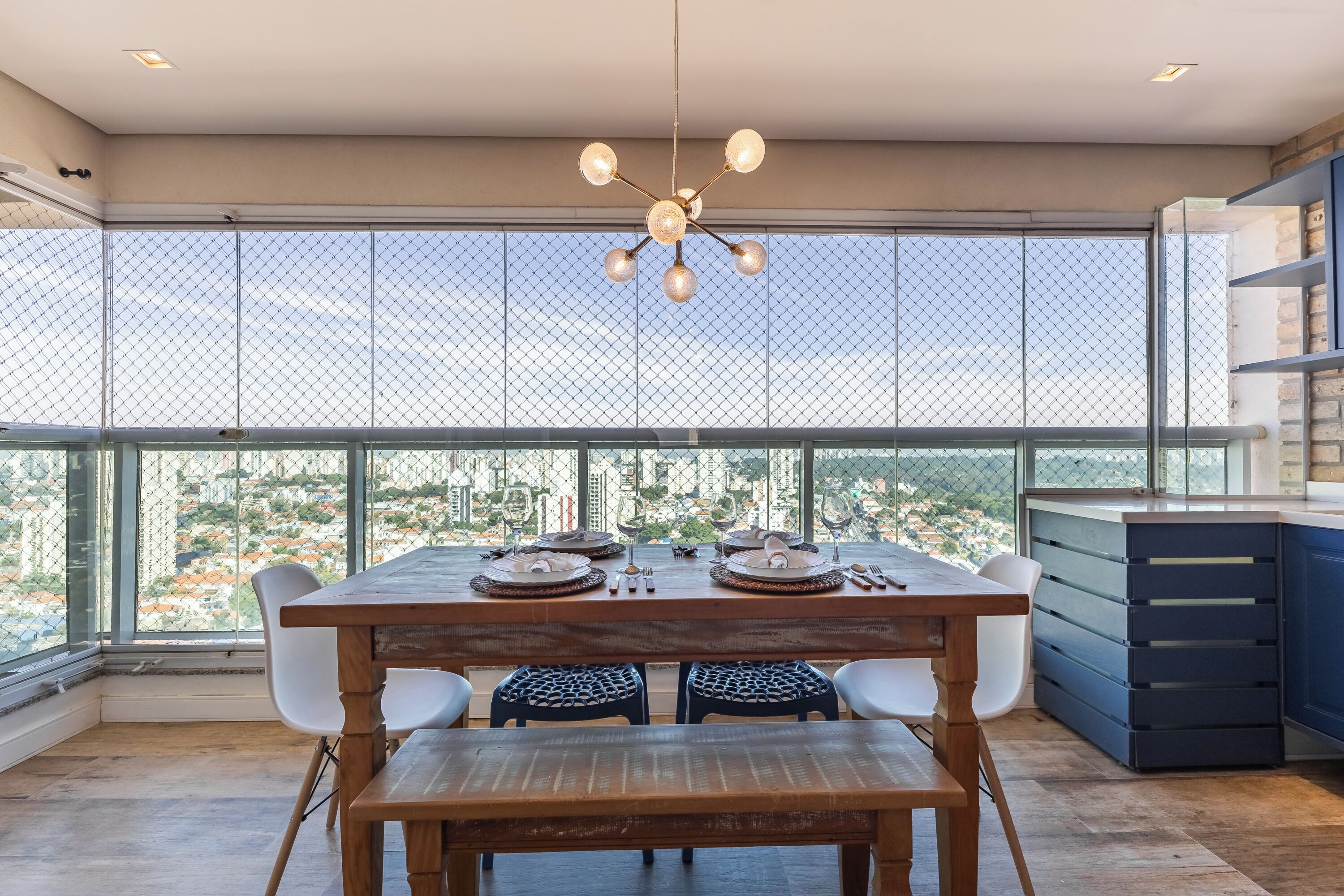 Un comedor con una mesa dispuesta para dos, un candelabro moderno y vistas a través de un ventanal con una barandilla metálica.