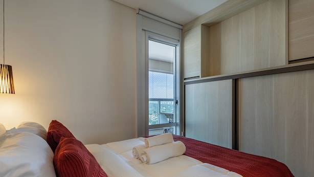 Habitación de hotel con cama, ventana con vistas y lámpara de pared.