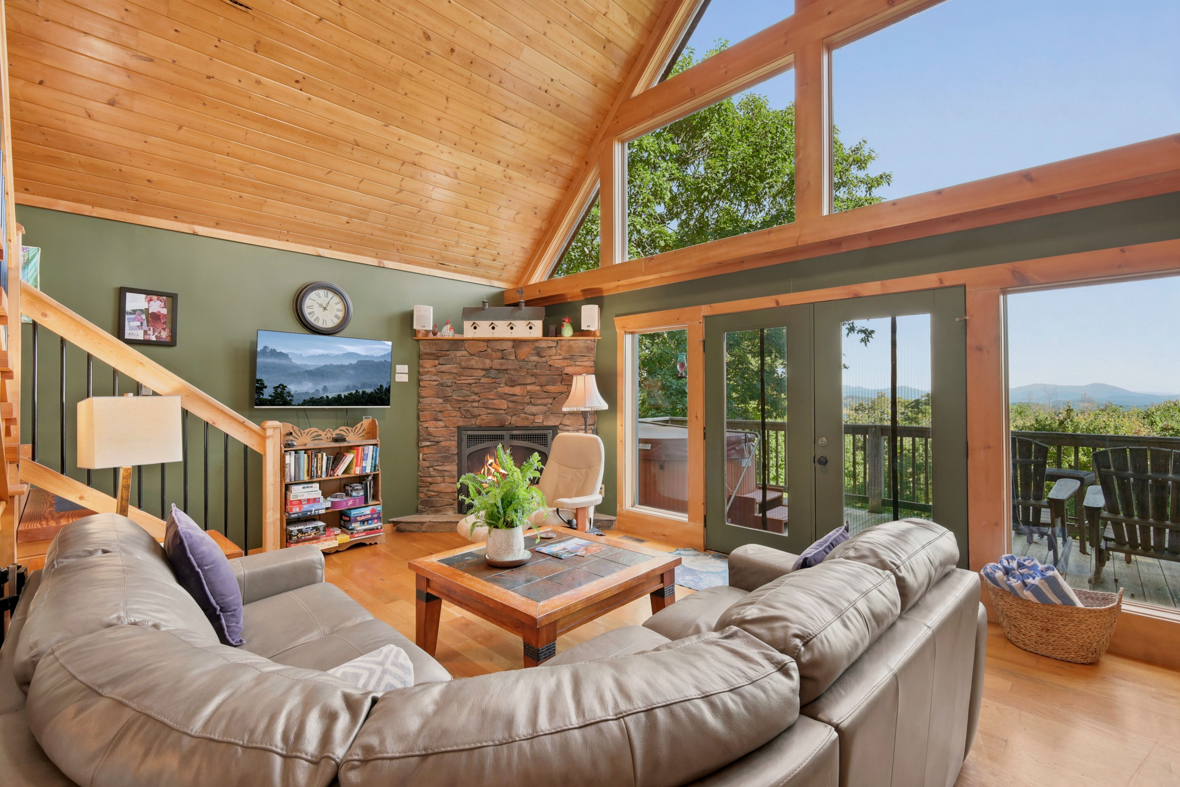 A spacious living room with a stone fireplace, a wooden ceiling, a large window, and a view of the outdoors.