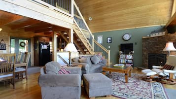 A spacious living area with a high ceiling, a fireplace, a staircase, and a cozy seating arrangement.