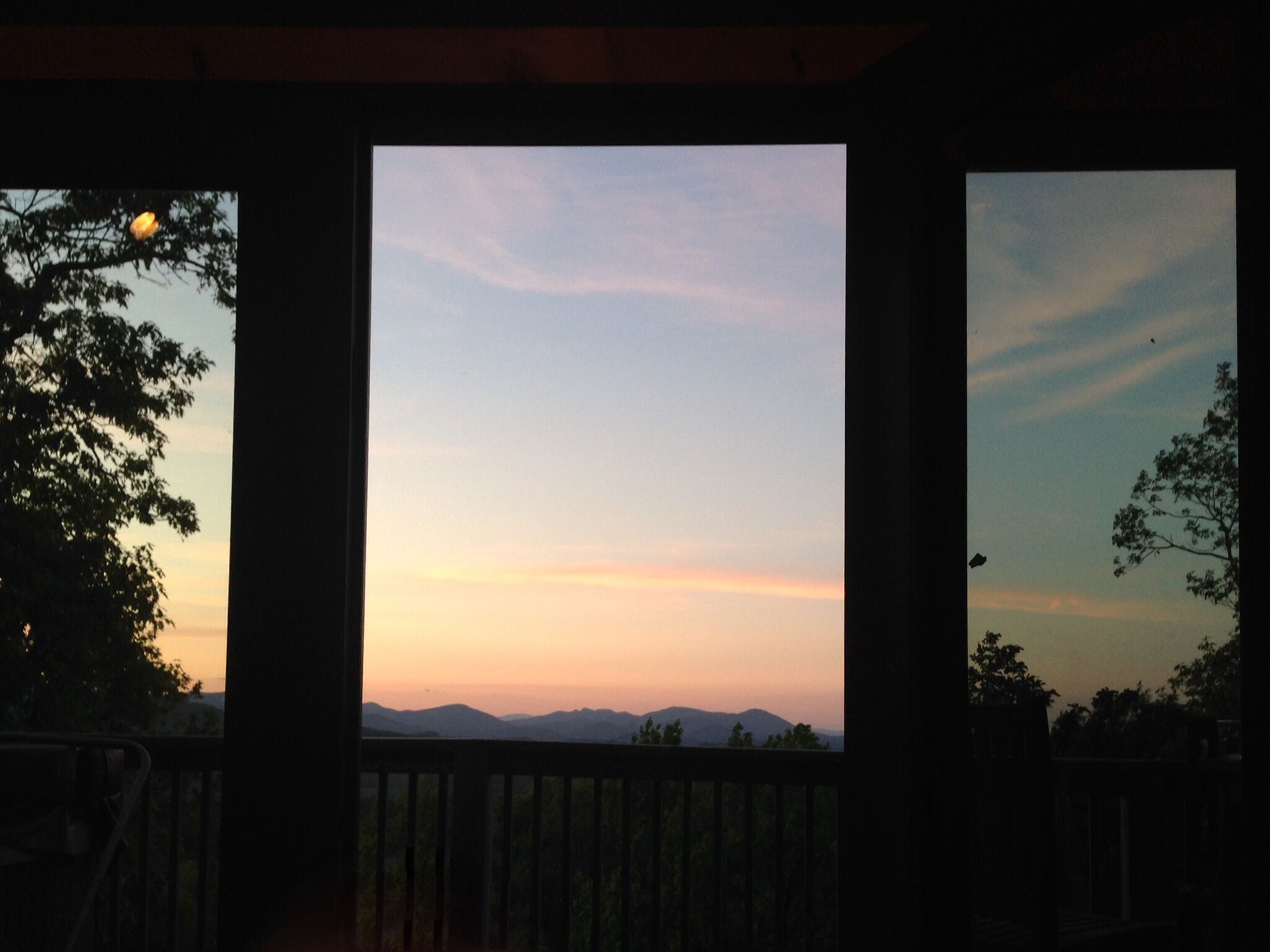 A view through a window with a wooden frame, overlooking a landscape with distant mountains and a clear sky.