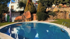 A swimming pool with a stone wall and a metal fence in the background.
