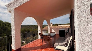 A covered outdoor area with a table and chairs, a grill, and a view of the landscape.
