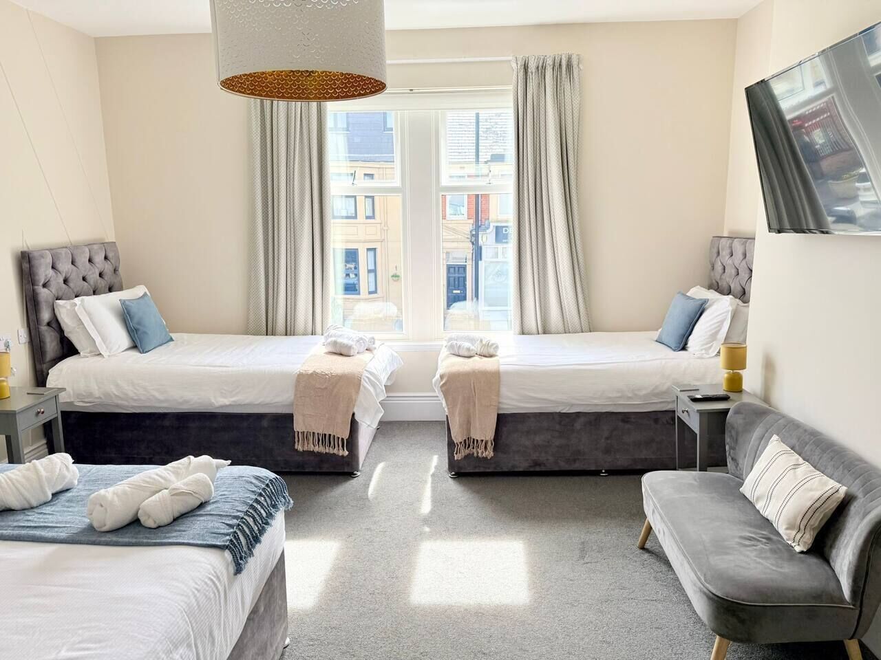 A hotel room with two beds, a sofa, a lamp, and a view of buildings through the window.