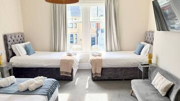A hotel room with two beds, a sofa, a lamp, and a view of buildings through the window.
