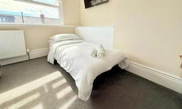 A single bed in a room with a radiator, a window, and a view of the outside.