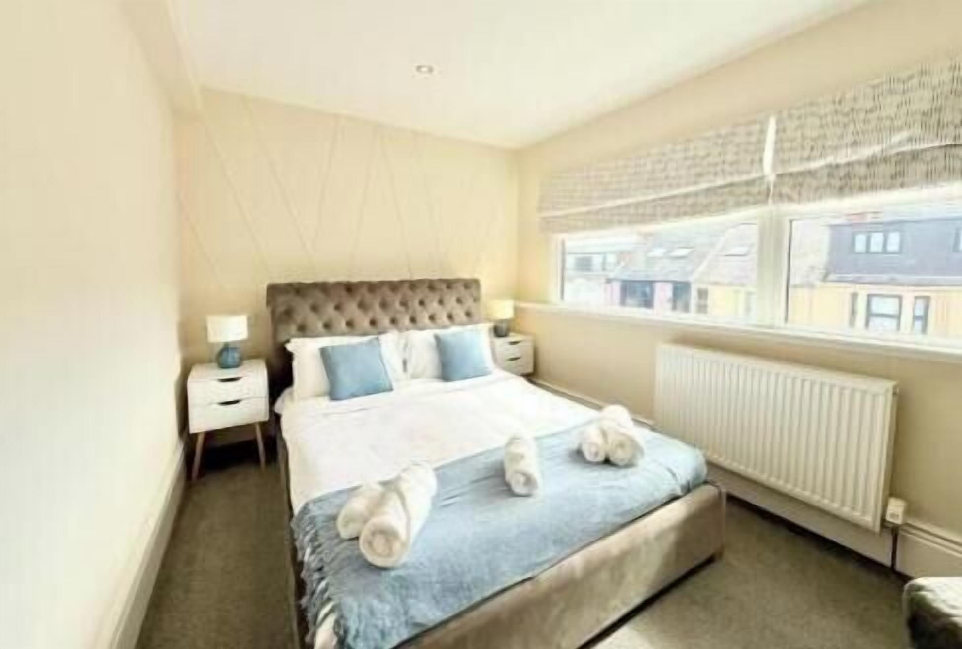 A bedroom with a large bed, bedside tables, a window with blinds, and a radiator.
