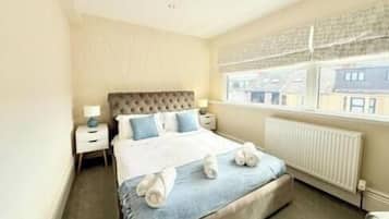 A bedroom with a large bed, bedside tables, a window with blinds, and a radiator.