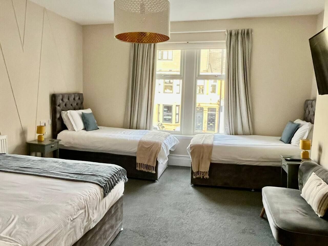 Habitación de hotel con dos camas, un sofá, una lámpara y vistas a edificios a través del ventanal.