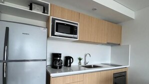 Una cocina moderna con un refrigerador de acero inoxidable, un microondas, una cafetera y armarios de madera.