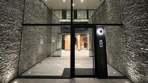 Un pasillo interior con puerta de vidrio que da a una zona de recepción, con pared texturizada e iluminación empotrada en el techo.