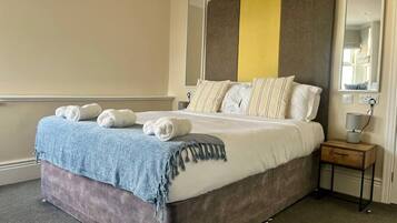 A neatly made bed with pillows and a blanket, a bedside table with a lamp, and a mirror on the wall.