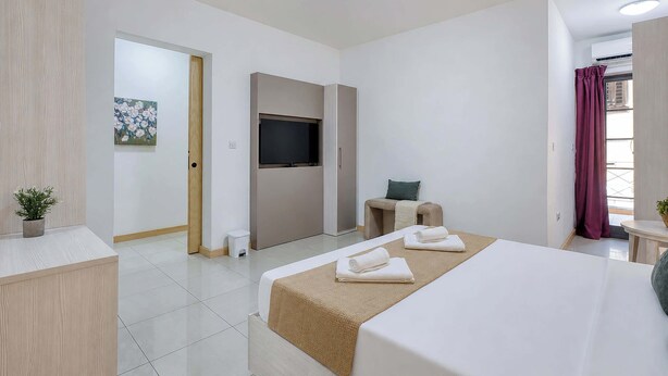 A modern hotel room with a bed, a TV, a small table, and a potted plant. - Belmonte Heights Flat 2BDR (Sliema)