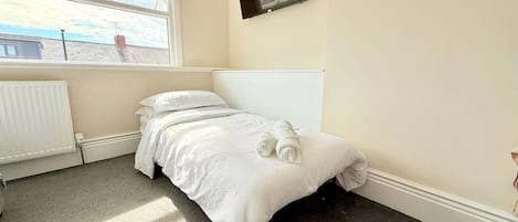 A bedroom with a bed, a radiator, a window, and a television on the wall.