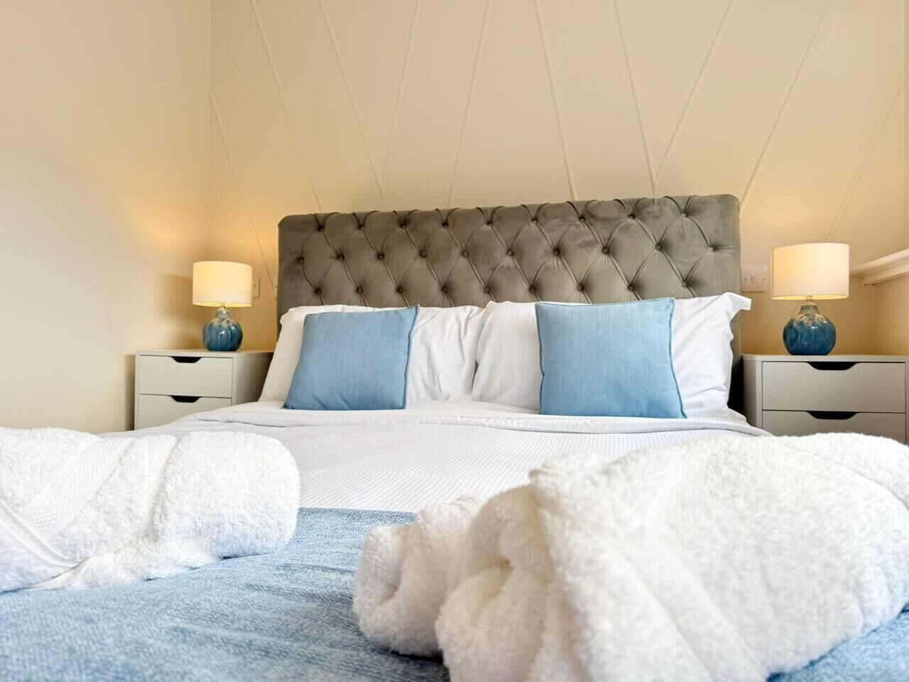 A neatly made bed with a tufted headboard, two bedside lamps, and a blue and white pillow arrangement.