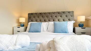 A neatly made bed with a tufted headboard, two bedside lamps, and a blue and white pillow arrangement.