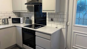 A kitchen with white cabinets, a black range hood, a microwave, a toaster, and an oven.