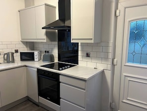 A kitchen with white cabinets, a black range hood, a microwave, a toaster, and an oven. - Bens Green, parking, spacious home, near the Peaks (South Yorkshire)