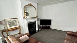 A living room with a brown leather sofa, a fireplace, a television, and a framed picture on a console table.
