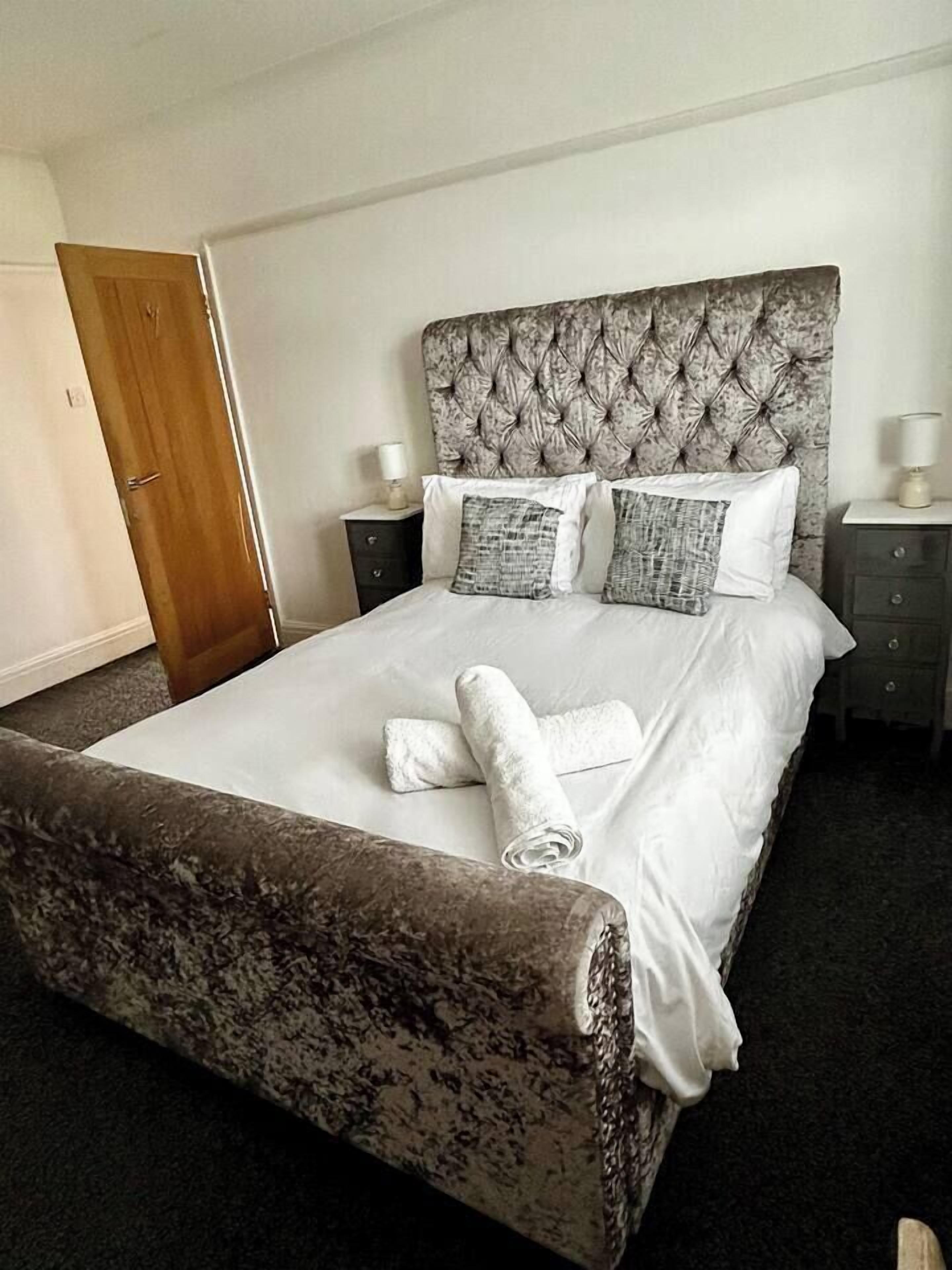 A neatly made bed with a tufted headboard, white bedding, and a brown accent bed runner.