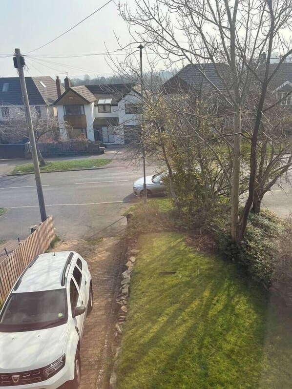 A residential street with houses, a parked white car, and a tree.