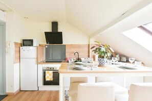 A modern kitchen with a dining area, equipped with a refrigerator, microwave, oven, and a black range hood. - Mulhouse's Golden Age (Mulhouse)