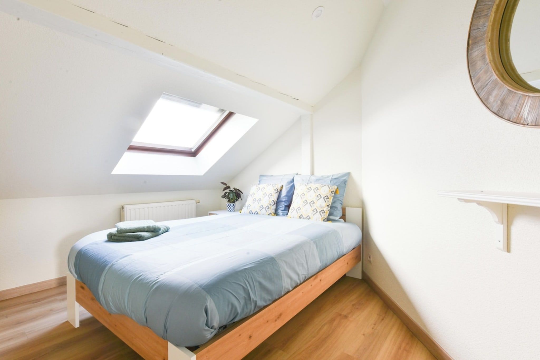 Een slaapkamer met dakraam, een bed met blauw beddengoed, een houten vloer en een witte radiator.