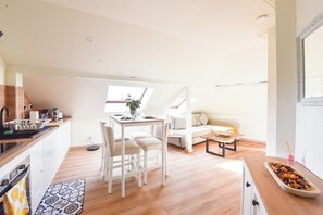 A modern kitchen with white cabinets, a dining area with a table and chairs, a sofa, and a small coffee table. - Apogee Mulhousienne - Cozy attic apartment, AC, Wi-Fi (Mulhouse)
