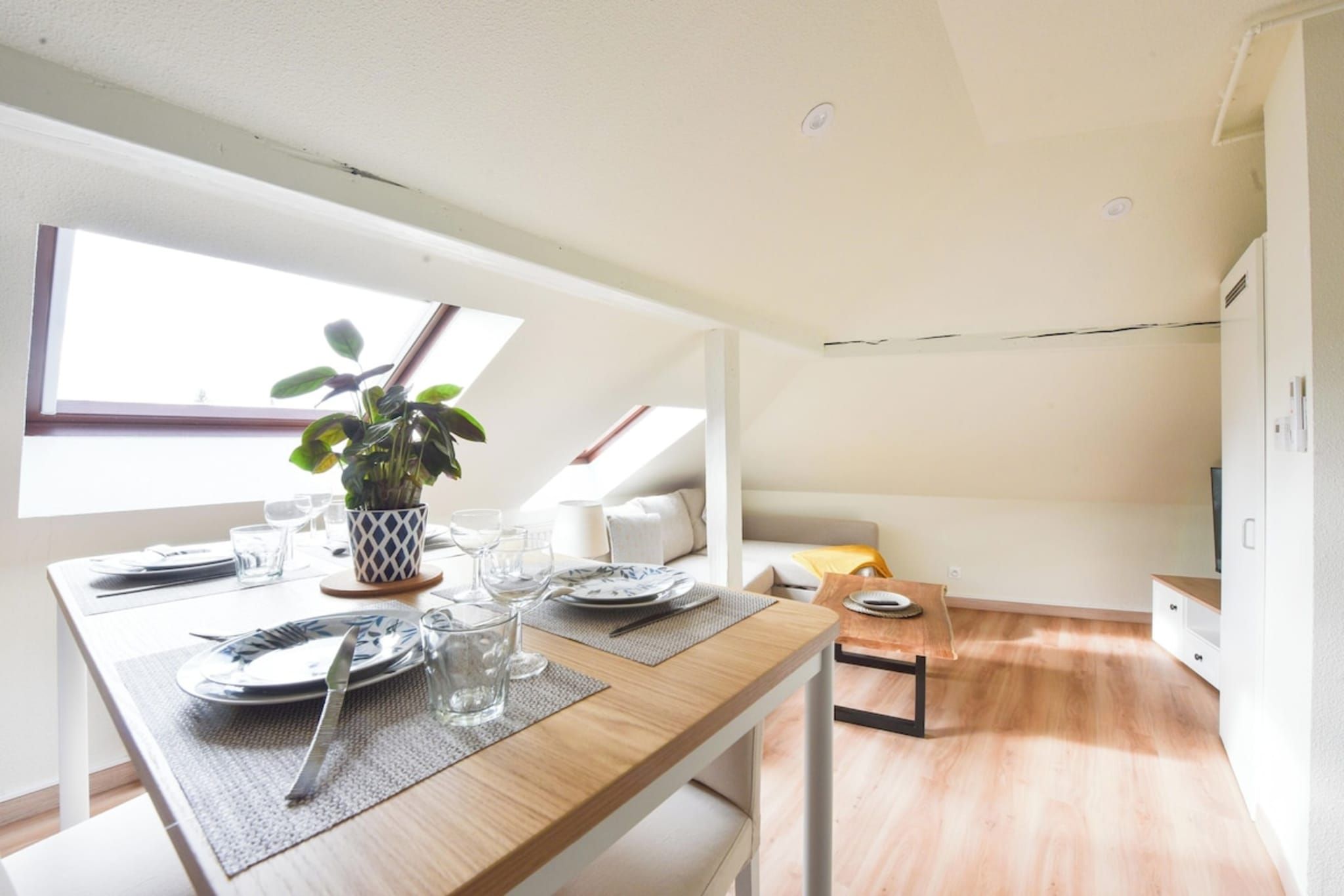 A dining area with a table set for two, a potted plant, and a view of the sky through a skylight.
