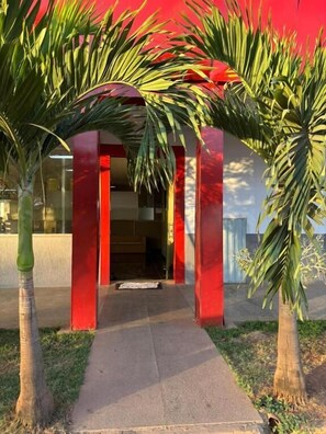 A building entrance with a red archway, a pathway leading to the entrance, and two palm trees on either side.