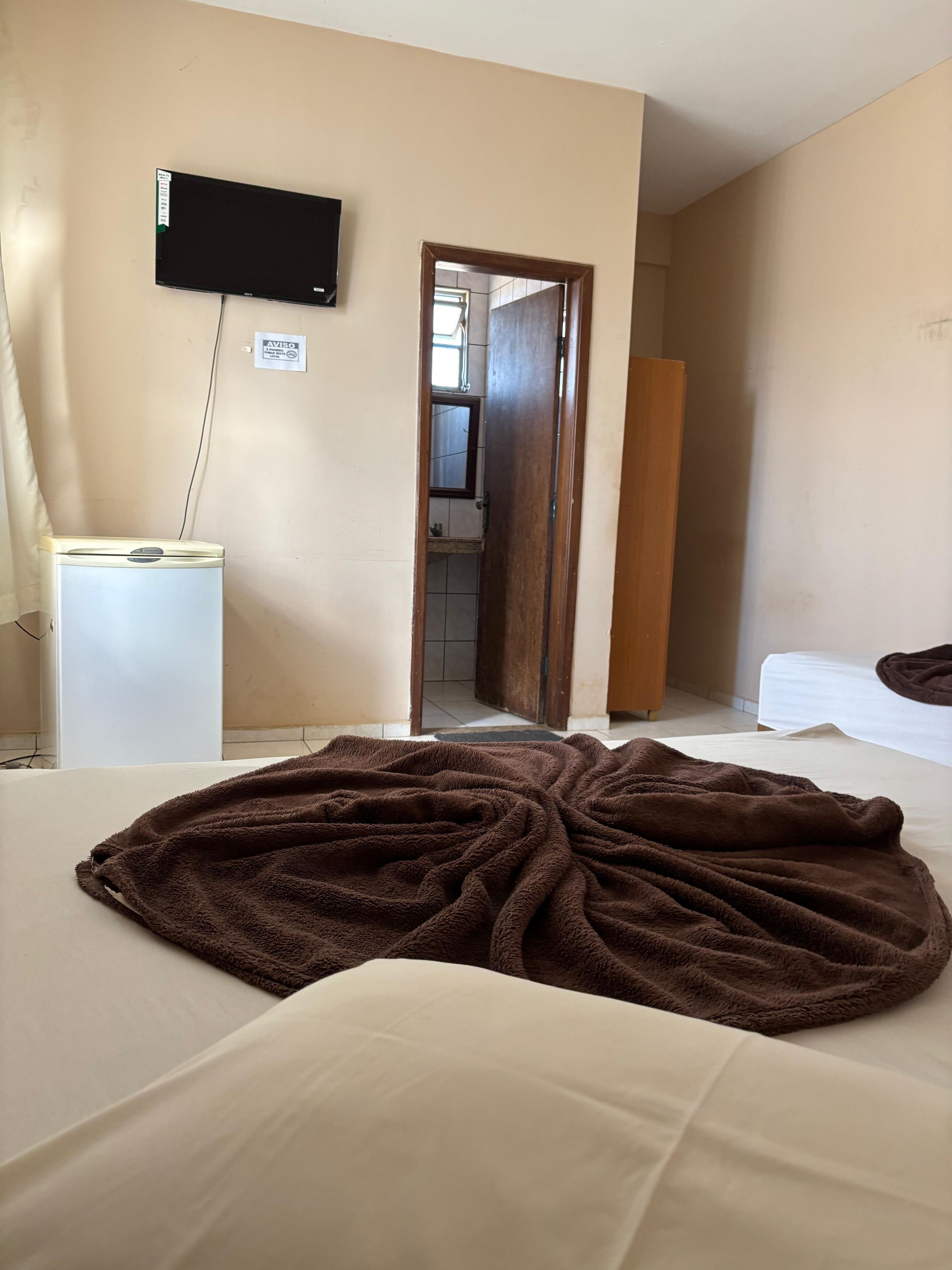 Une chambre d’hôtel comprenant un lit, un téléviseur fixé au mur, un petit bureau et une porte donnant accès à une salle de bain.