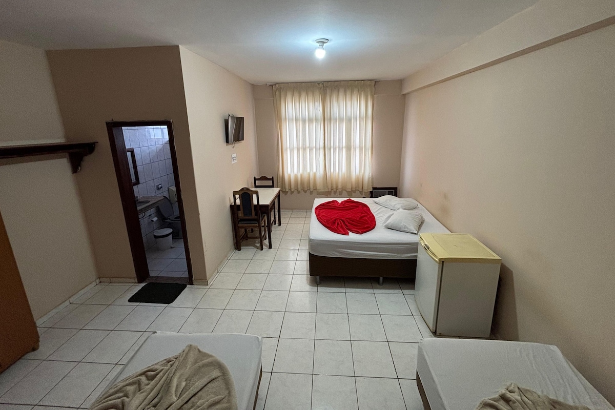 Habitación de hotel con cama, escritorio, silla, televisor y un pequeño armario.