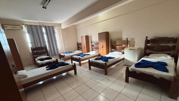 A hotel room with four single beds, a wooden wardrobe, a desk, and a window with curtains.