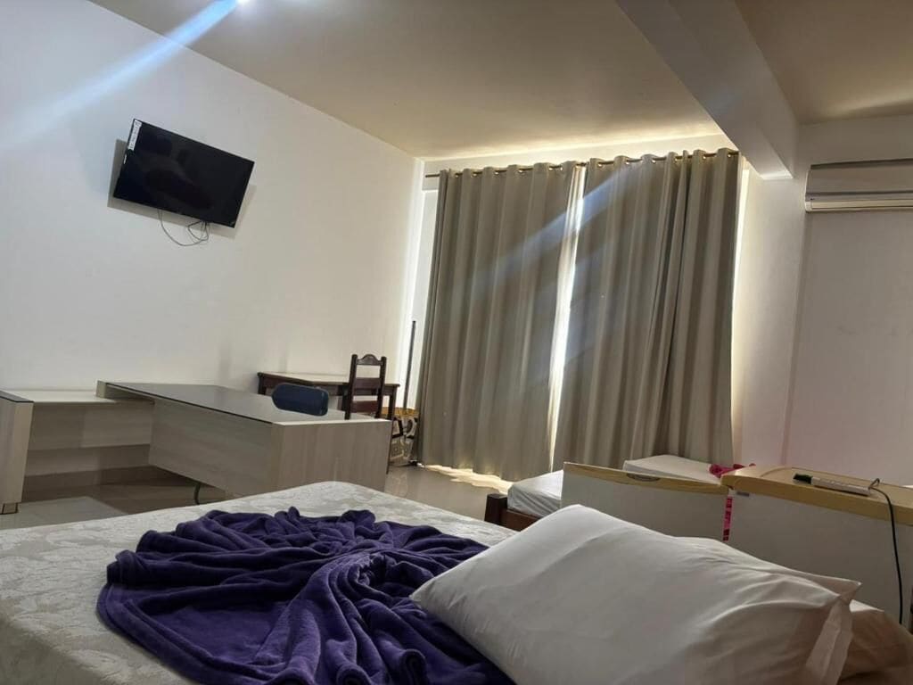 Habitación de hotel con cama, escritorio, silla, televisor montado en la pared y ventana con cortinas.