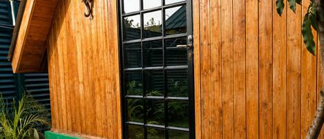A wooden cabin with a glass door, a sign above the door, and a set of wooden steps leading to the entrance.