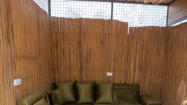 A room with a sectional sofa, a glass coffee table, and a bamboo wall.