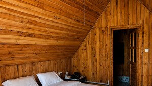 Habitación con paneles de madera, una cama individual, una mesita de noche y una puerta que da a otra habitación.