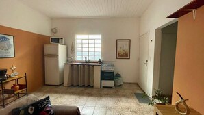 Cozinha compacta com geladeira, micro-ondas, fogão e pia. Há uma janela que oferece luz natural e uma porta que dá para outro cômodo.