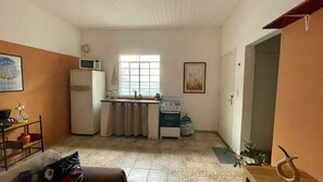 Eine kleine Küche mit Kühlschrank, Mikrowelle, Herd und Spüle. Ein Fenster lässt Tageslicht herein, und eine Tür führt in einen weiteren Raum.
