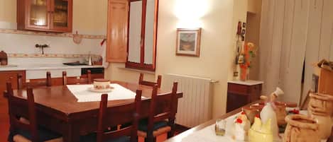 Un comedor con mesa y sillas de madera, una cocina al fondo y una ventana con cortinas.