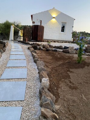 A pathway leading to a white building with a light fixture on the roof, surrounded by rocks and pebbles. - Antony's House (Orosei)