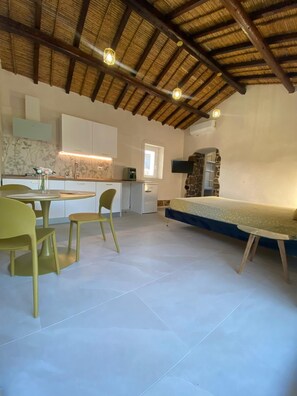 A compact living space with a kitchenette, a dining area with chairs, a bed, and a stone wall. - Antony's House (Orosei)