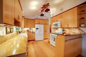 Una cocina con armarios de madera, encimera de granito, refrigerador, microondas y estufa.