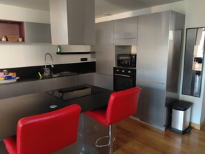 A modern kitchen with a black countertop, stainless steel appliances, and red bar stools. - L'Instant Sud in Châteauneuf-de-Grasse (Châteauneuf-Grasse)