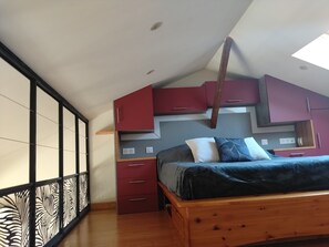 A bedroom with a sloped ceiling, a bed with a dark blue blanket, red and grey cabinets, and a wooden headboard. - L'Instant Sud in Châteauneuf-de-Grasse (Châteauneuf-Grasse)
