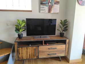 A wooden entertainment center with a flat-screen TV, two potted plants, and a wall clock. - L'Instant Sud in Châteauneuf-de-Grasse (Châteauneuf-Grasse)